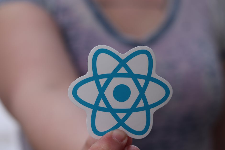 A person holding a sticker featuring a blue and white atomic model symbol, with a blurred background of a person wearing a purple top, highlighting the focus on the sticker. The atomic symbol has inte